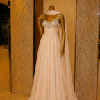 Beige evening gown with intricate top on a mannequin against a beige wall.