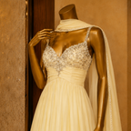 Mannequin wearing a beige evening gown with intricate detailing against a brown background