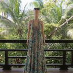 Mannequin wearing a long, patterned dress on a wooden deck with tropical foliage in the background