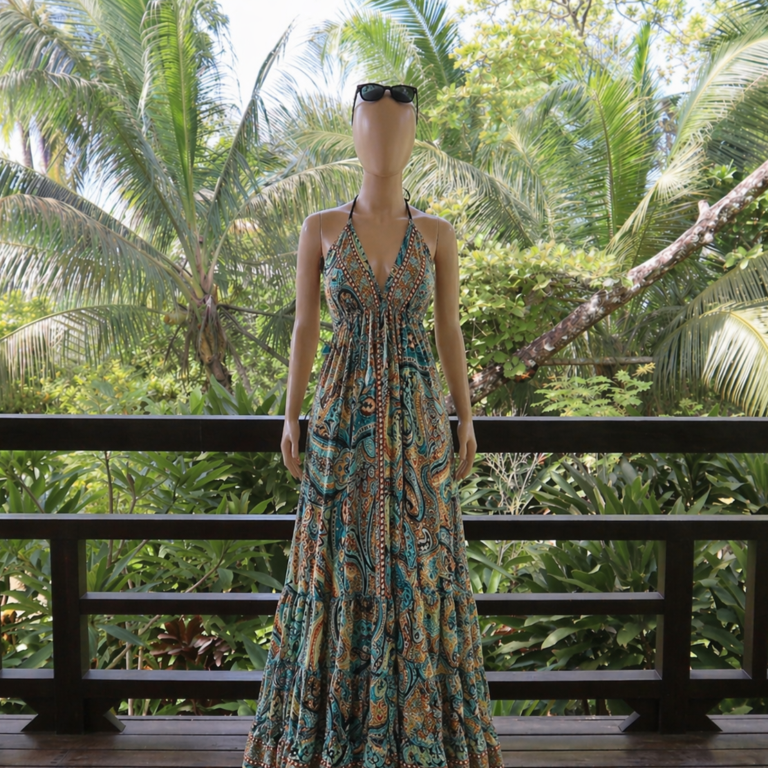 Mannequin wearing a long, patterned dress on a wooden deck with tropical foliage in the background