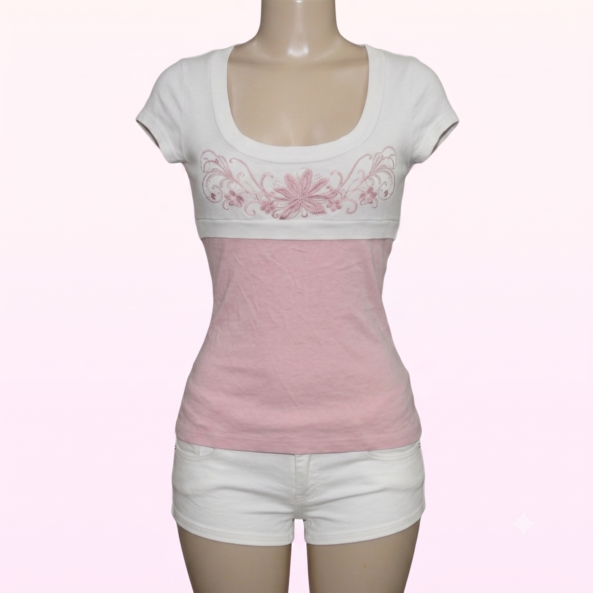 A women's short-sleeve scoop-neck top displayed on a mannequin, featuring a white upper section with pink floral embroidery across the chest and a solid light pink lower section, paired with white shorts.