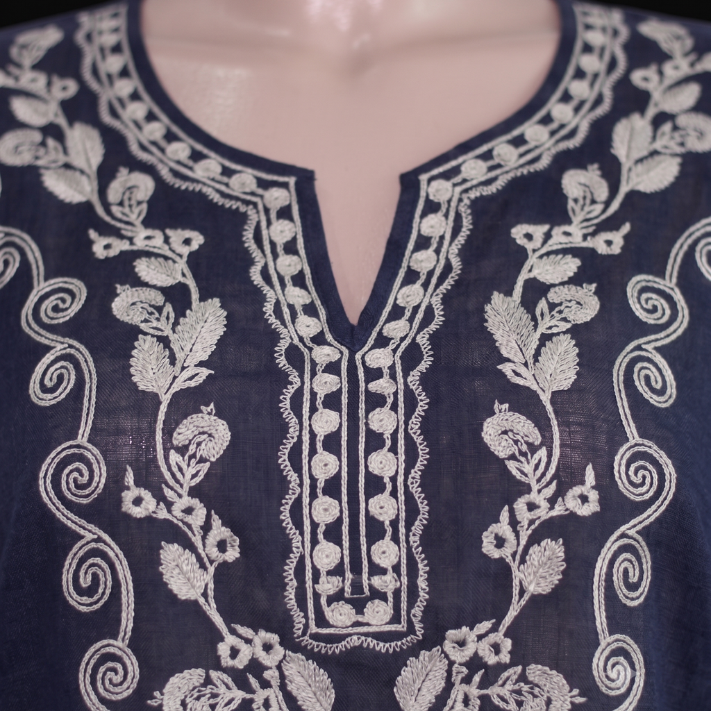 Close-up of a navy blue embroidered tunic top displayed on a mannequin torso, featuring intricate white floral and scroll embroidery around a split neckline.