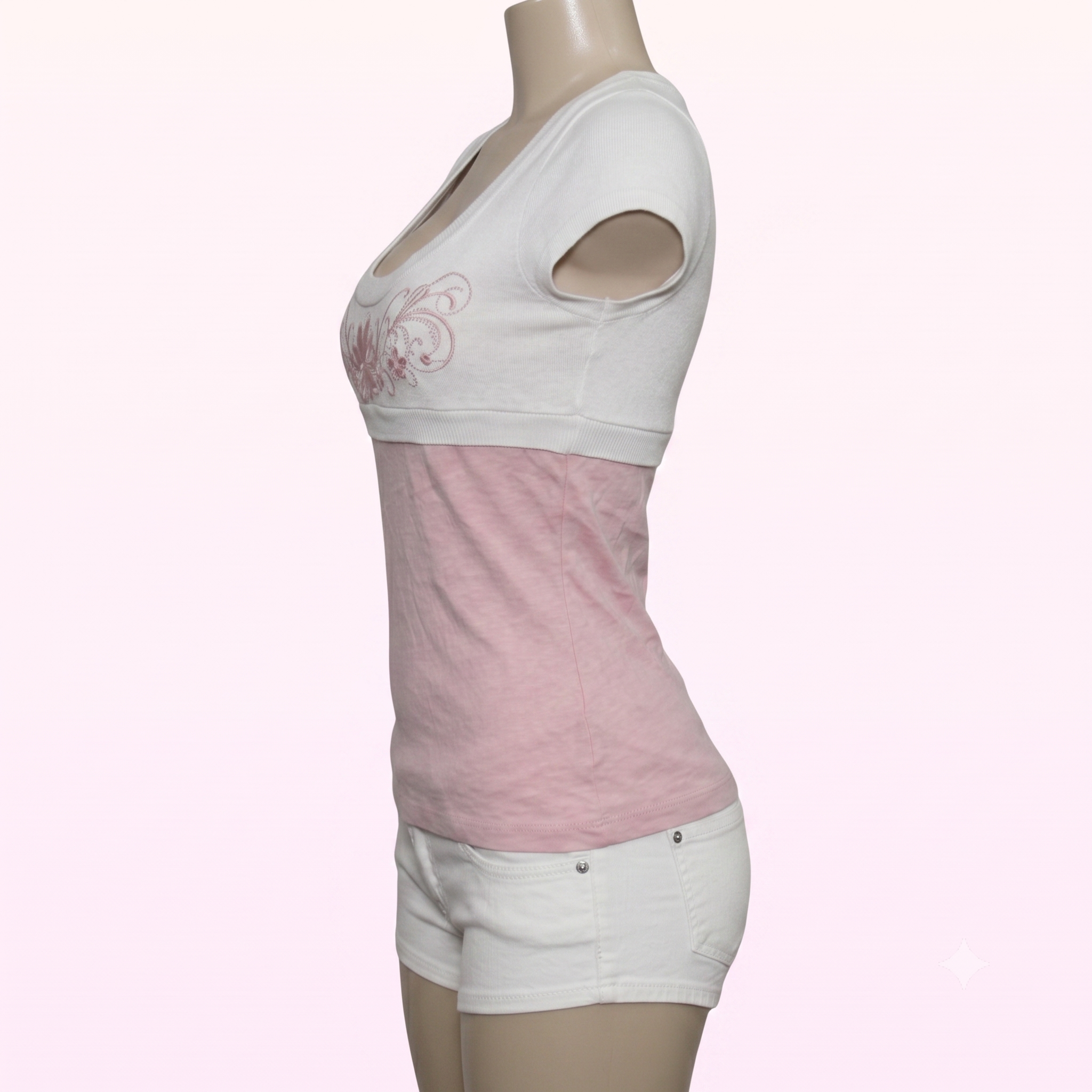 A women's short-sleeve crop top in a colorblock design of white and light pink, shown on a mannequin torso. The top features a white upper section with a pink butterfly graphic on the left chest, a solid pink middle section, and a white lower hem with cutout details in the sleeves.